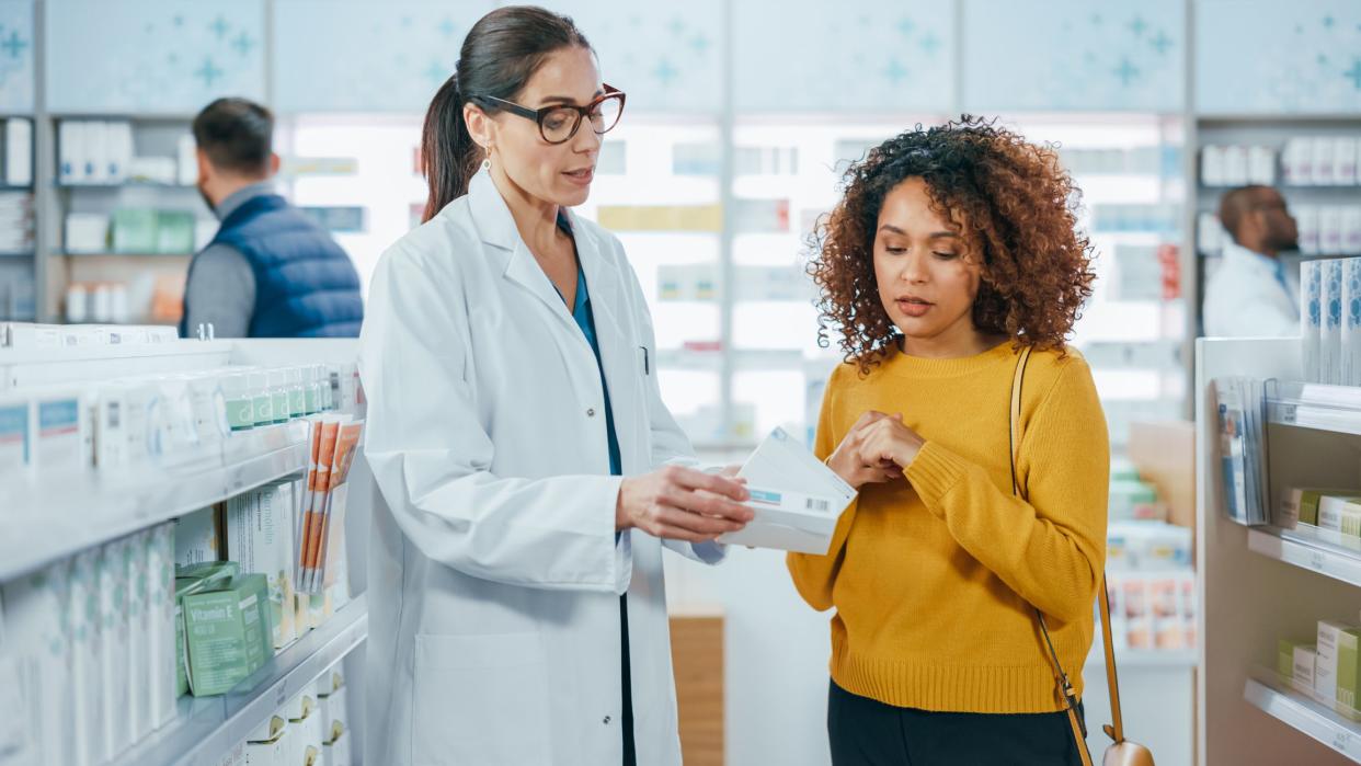 Pharmacy: Professional Caucasian Pharmacist Helping Beautiful Black Female Customer with Medicine Recommendation, Advice, Talking. Drugstore with Full of Drugs, Pills, Health Care, Beauty Products
