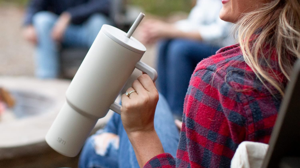 woman holding simple modern tumbler, a Stanley alternative, next to bonfire outside