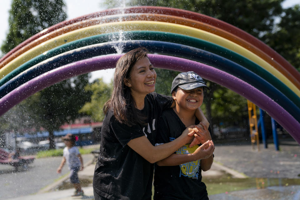 Monica Muquinche and her son Sebastian plan in a sprinkler at a playground in their neighborhood in the Brooklyn borough of New York, Thursday, Aug. 26, 2021. Muquinche, whose husband disappeared in 2020 while trying to reach the U.S., is part of an extraordinary wave of Ecuadorians coming in the United States. (AP Photo/John Minchillo)