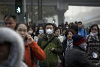 People, some wearing masks for protection against the pollution, walk across a traffic intersection at the Central Business District in Beijing, Tuesday, Nov. 13, 2018. Chinese Premier Li Keqiang says the country needs reforms to support business to help drive growth as it weathers a trade war with the U.S., rather than more economic stimulus. Li said Tuesday in Singapore that China can energize its slowing economy by adjusting policies, such as streamlining bureaucratic procedures like business registrations, taxes and fees. (AP Photo/Andy Wong)