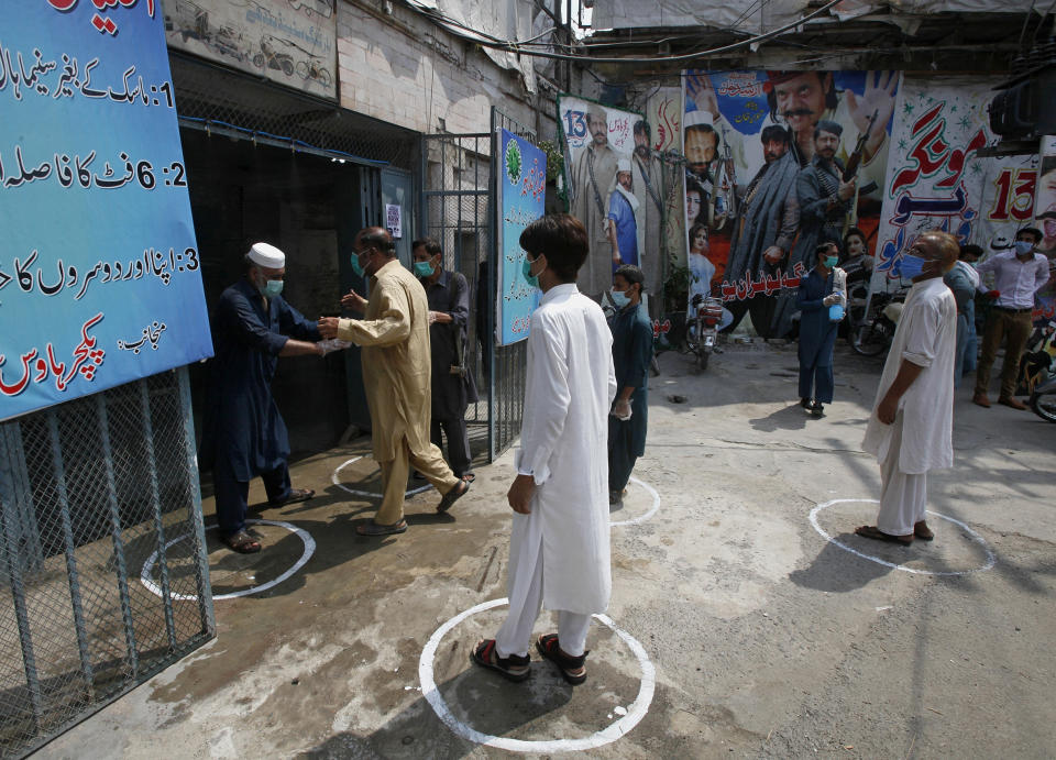 People wear face masks and keep social distancing as they enter a cinema following an ease in restrictions that had been imposed to help control the coronavirus, in Peshawar, Pakistan, Monday, Aug. 10, 2020. Pakistan's daily virus infection rate has stayed under 1,000 for more than four weeks prompting the government to further ease restrictions for restaurants, parks, gyms and cinemas. (AP Photo/Muhammad Sajjad)