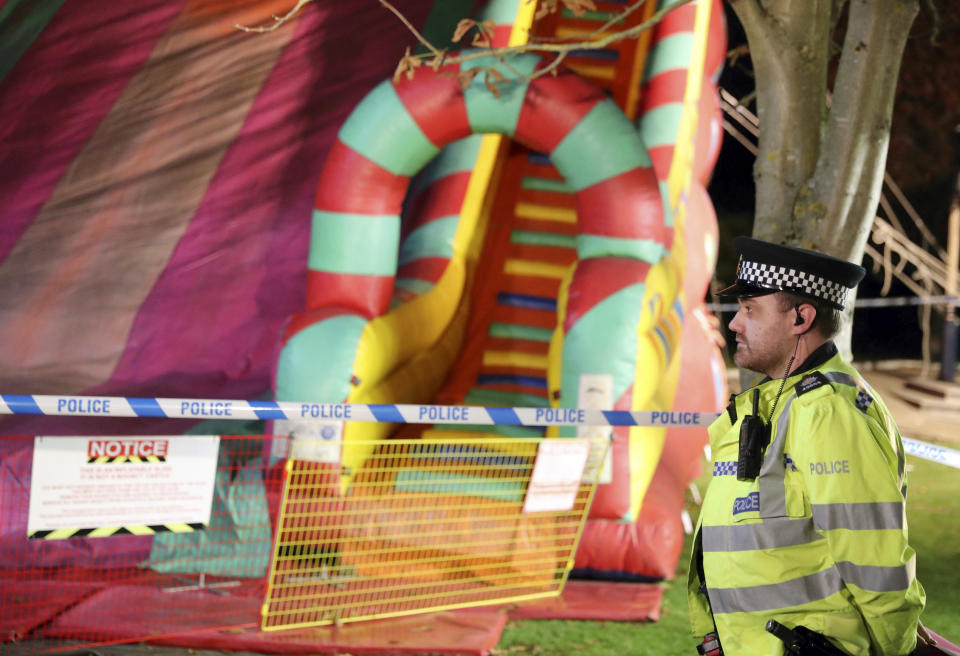 A police officer stands near an inflatable slide at a fireworks funfair in Woking Park, south England, Saturday Nov. 3, 2018. British police say seven of the eight children hurt when they fell from an inflatable slide at a fair in southern England have been discharged from the hospital. (Andrew Matthews/PA via AP)