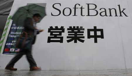 A man holding an umbrella walks past the logo of Softbank Corp at its branch in Tokyo April 22, 2014. REUTERS/Yuya Shino