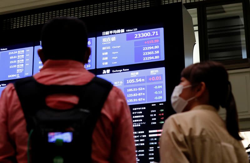 TV crews talk in front of a large screen showing stock prices at the Tokyo Stock Exchange in Tokyo