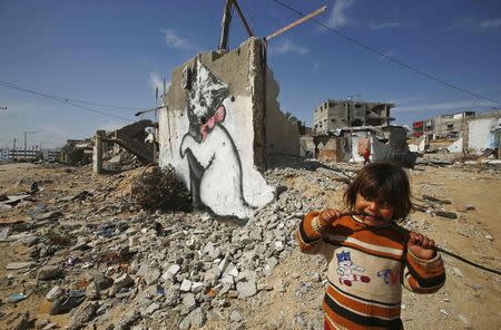 A Palestinian girl looks on as a mural of a playful-looking kitten, presumably painted by British street artist Banksy, is seen on the remains of a house that witnesses said was destroyed by Israeli shelling during a 50-day war last summer, in Biet Hanoun town in the northern Gaza Strip February 26, 2015. REUTERS/Suhaib Salem