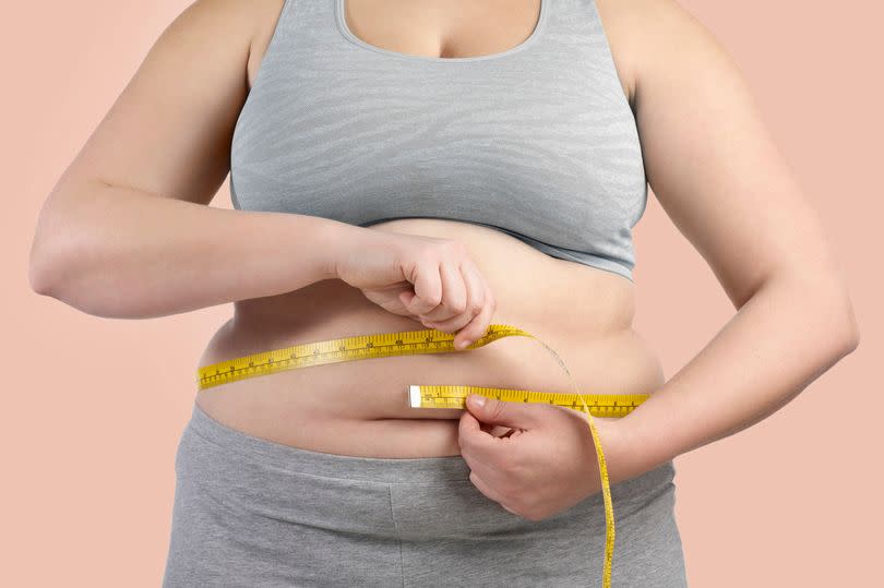 Overweight woman measuring her waist with a tape measure