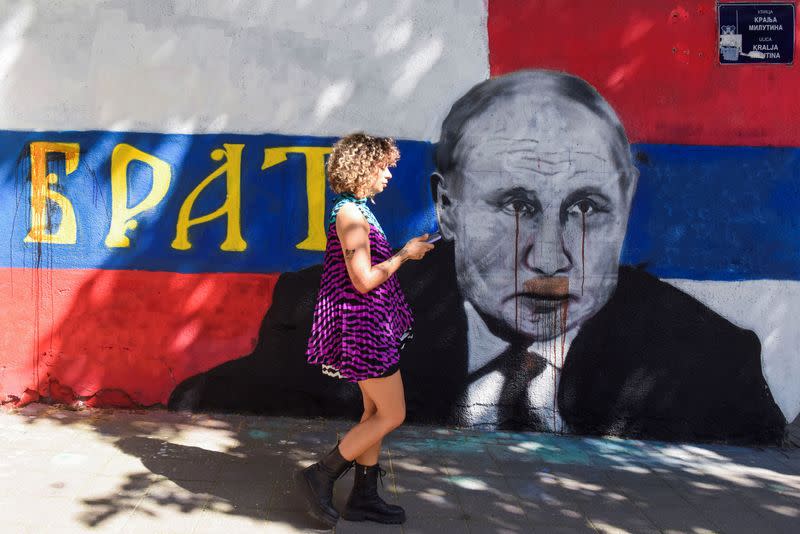 A woman walks next to a mural of Russian President Vladimir Putin, which has been vandalised with red spray paint, in Belgrade