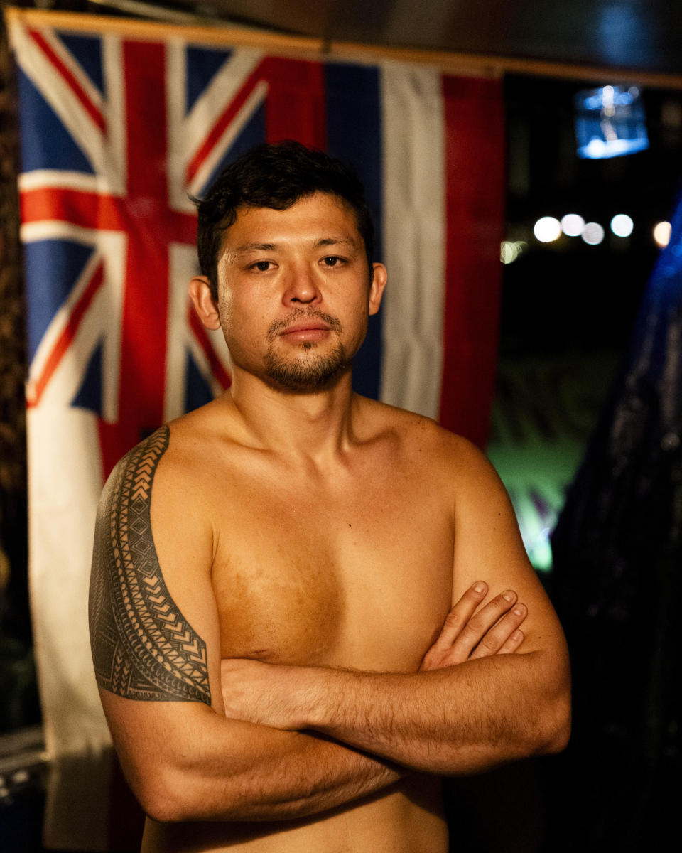 De Andre Makakoa, who lost his home to the Lahaina wildfire, poses for a portrait inside his tent at a housing protest on Kaanapali Beach Wednesday, Dec. 6, 2023, in Lahaina, Hawaii. A group of survivors is camping on the resort beach to protest and raise awareness for better long-term housing options for those displaced. Residents and survivors still dealing with the aftermath of the August wildfires in Lahaina have mixed feelings as tourists begin to return to the west side of Maui, staying in hotels still housing some displaced residents. (AP Photo/Lindsey Wasson)