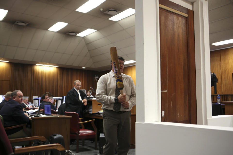 Forensic investigator Johannes Vermeulen, with a cricket bat in hand, demonstrates on a mock-up toilet and door details of how the door could have been broken down, during the trial of Oscar Pistorius in court during the second week of his trial in Pretoria, South Africa, Wednesday, March 12, 2014. Pistorius is charged with the shooting death of his girlfriend Reeva Steenkamp on Valentine's Day in 2013. At center back is prosecutor Gerrie Nel. (AP Photo/Alexander Joe, Pool)