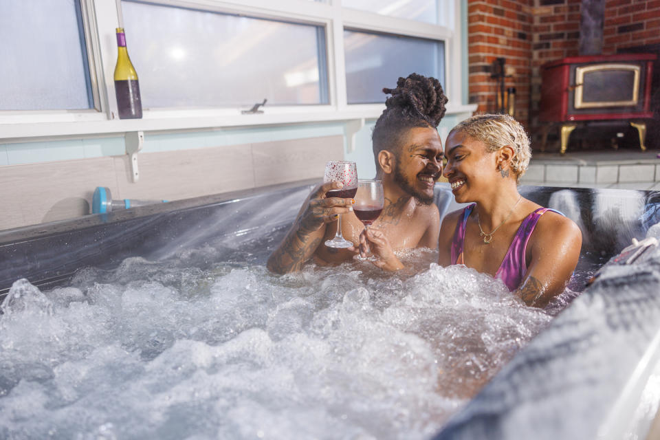 A couple, smiling and holding wine glasses, enjoys a relaxing moment in a hot tub