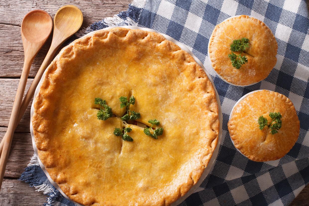 One large and two small pumpkin pot pies on a blue checkered napkin with two wooden spoons on a wooden table