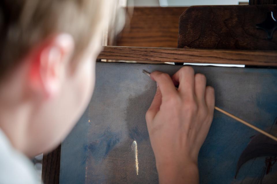 Painting Conservator Sara Boesen uses a hand made cotton swab with saliva as she works to restore a painting at her studio in Des Moines, Friday, July 8, 2022.