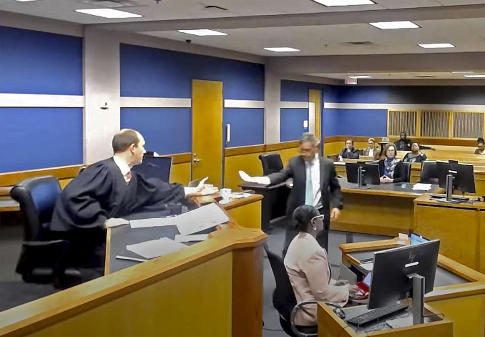 In this frame grab from video, Brian Rafferty, attorney for Sidney Powell, hands Judge Scott McAfee plea documents as Powell attends a hearing on Thursday, Oct. 19, 2023 at the Fulton County Courthouse in Atlanta. Powell, former attorney for former President Donald Trump, pleaded guilty in the Georgia election interference case and will serve six years probation, pay a fine, and she will be required to testify in future trials. (Fulton County Court/Pool Photo via AP)