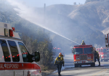 Firefighters spray water from a fire truck as they battle the Woolsey fire in West Hills, Southern California, U.S. November 11, 2018. REUTERS/Mario Anzuoni