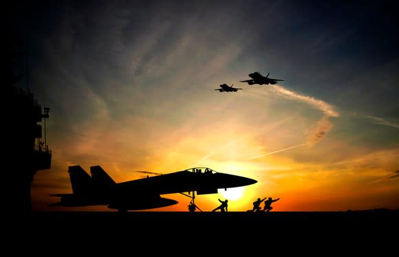 Fighter jet taking off from aircraft carrier at sunset.