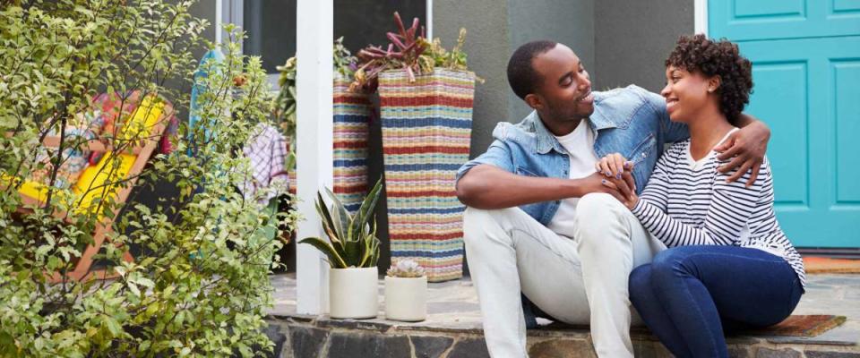 Young couple sit looking at each other outside their house