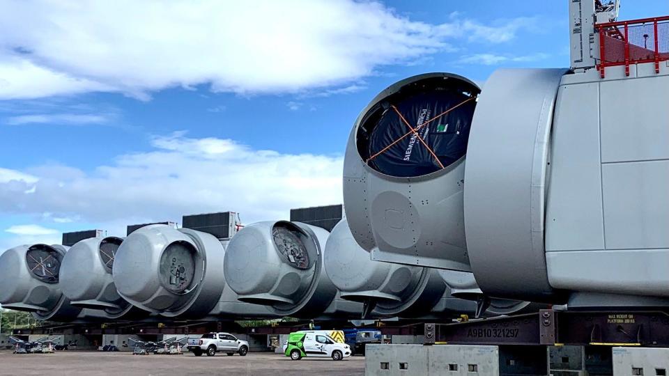 Wind turbine 'nacelles' - Very large components of wind farm generators towering over parked vans before turbines are constructed
