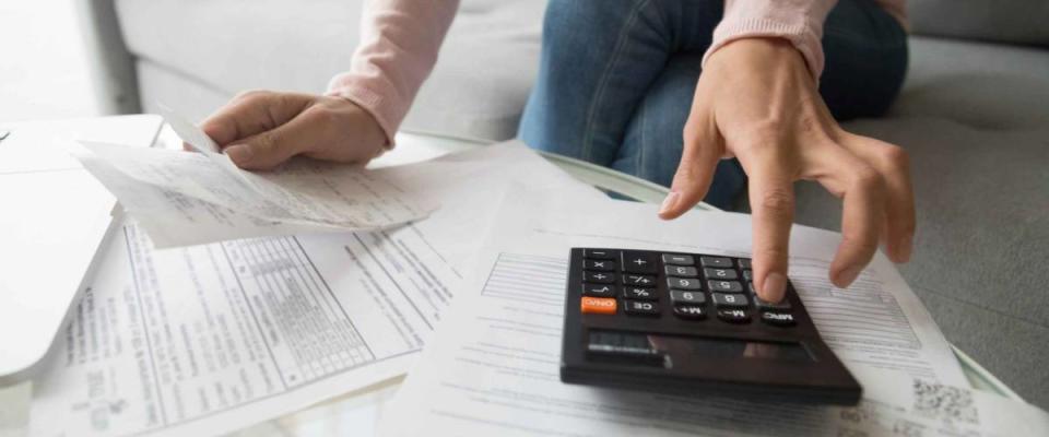 Woman renter holding paper bills using calculator to determine affordable student loan payment.