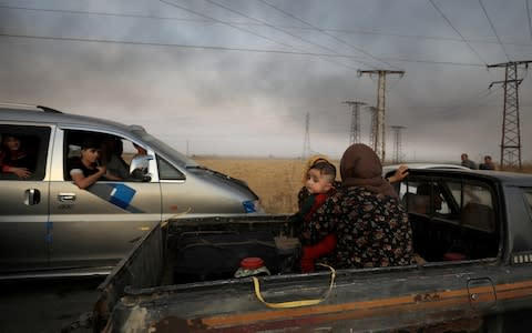 A woman with a baby sits at a back of a truck as they flee Ras al Ain town - Credit: Reuters