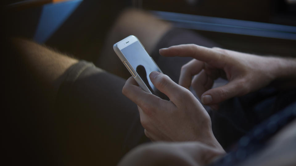 Close-up of hands holding smartphone inside car at sunset