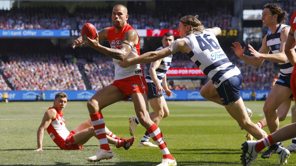 Buddy Franklin handballs as Geelong's Mark Blicavs attempts a tackle.