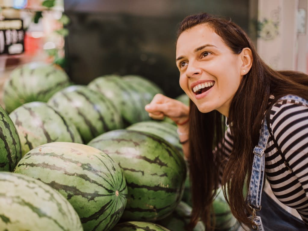  A woman listens as she knocks on a watermelon with her fist. 