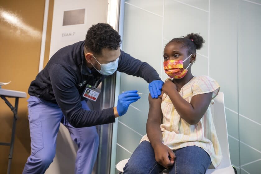 TUSTIN, CA - NOVEMBER 04: Niko Barner, 8, of Chino, left, receives a vaccination from Christopher King, 31, LVN, left, as he prepares to give her a vaccination at Kaiser Permanente Tustin Ranch Vaccination Clinic on Thursday, Nov. 4, 2021 in Tustin, CA. Following FDA and CDC approval of the Pfizer COVID-19 vaccine for younger children, Kaiser Permanente health care professionals will administer the first of two shots to six children ranging in age between 5-11 to protect them against contracting Covid-19. (Francine Orr / Los Angeles Times)