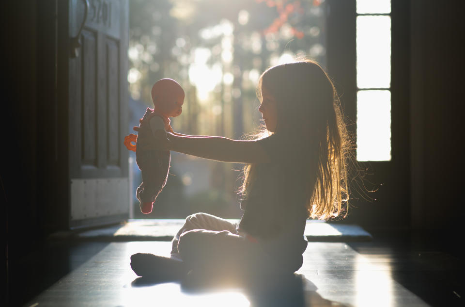 Young girl sitting in a hallway holding her baby doll. Backlit.