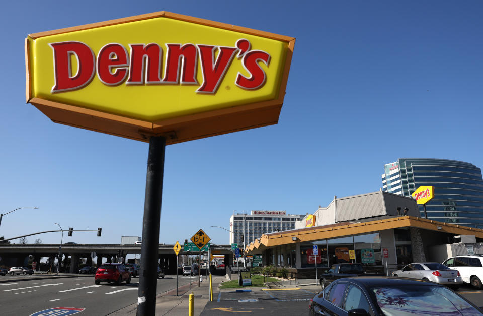 A Denny's sign against a blue sky advertises a diner location in California.