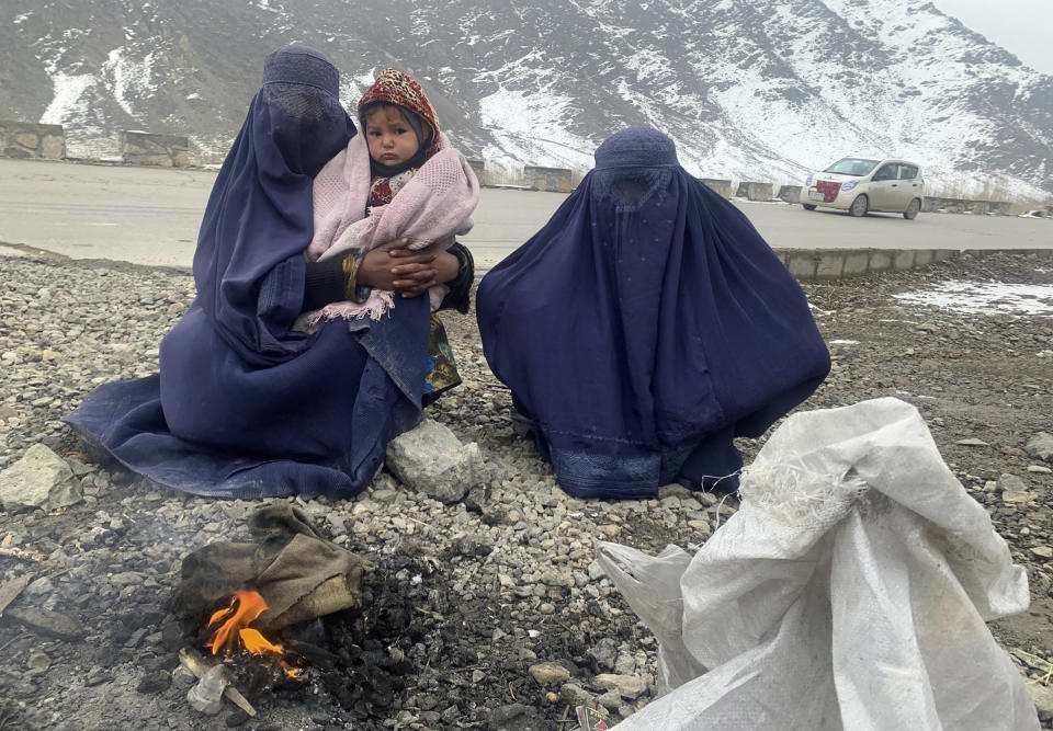 Gulnaz, left, keep her 18-month-old son warm themselves as they wait for alms in the Kabul - Pul-e-Alam highway eastern Afghanistan, Tuesday, Jan. 18, 2022. The Taliban's sweep to power in Afghanistan in August drove billions of dollars in international assistance out of the country and sent an already dirt-poor poor nation, ravaged by war, drought and floods, spiralling toward a humanitarian catastrophe. (AP Photo/Kathy Gannon)