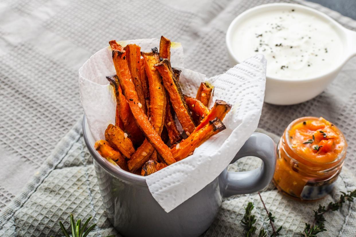Healthy baked carrot fries in a paper towel and grey mug with two dressings on matching grey linen and herbs