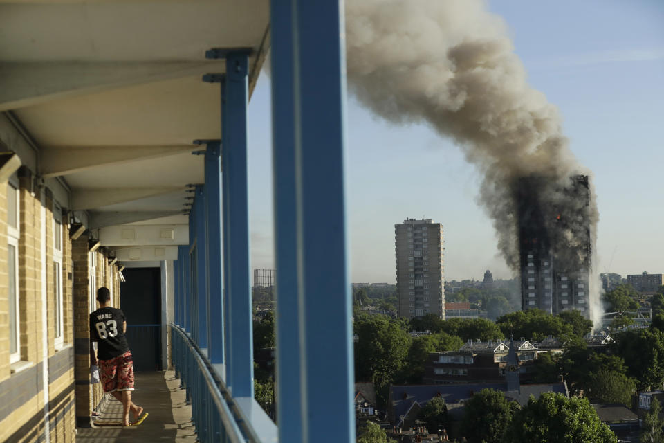 FILE - In this June 14, 2017, file photo, a resident in a nearby building watches smoke rise from a building on fire in London. An American lawyer known for winning huge legal awards over deadly construction accidents plans to hold a news conference in Philadelphia on the 2017 apartment fire in London that killed 72 people. The BBC has reported that more than 100 people plan to join a product liability lawsuit targeting U.S. companies that make products used at the complex. (AP Photo/Matt Dunham, File)