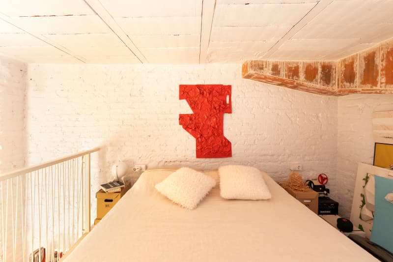 Painted white brick loft bedroom with textured art over bed and some exposed wood