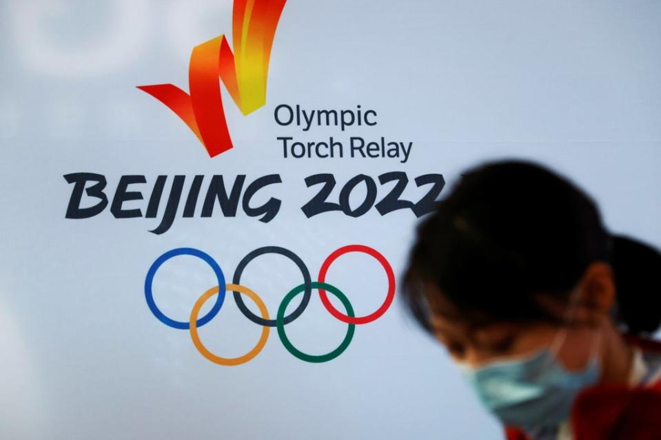 A woman wearing a face mask stands in front of the logo of the Beijing 2022 Winter Olympics before the Olympics flame exhibition tour at Beijing University of Posts and Telecommunications, in Beijing, China on 9 December 2021 (Reuters)