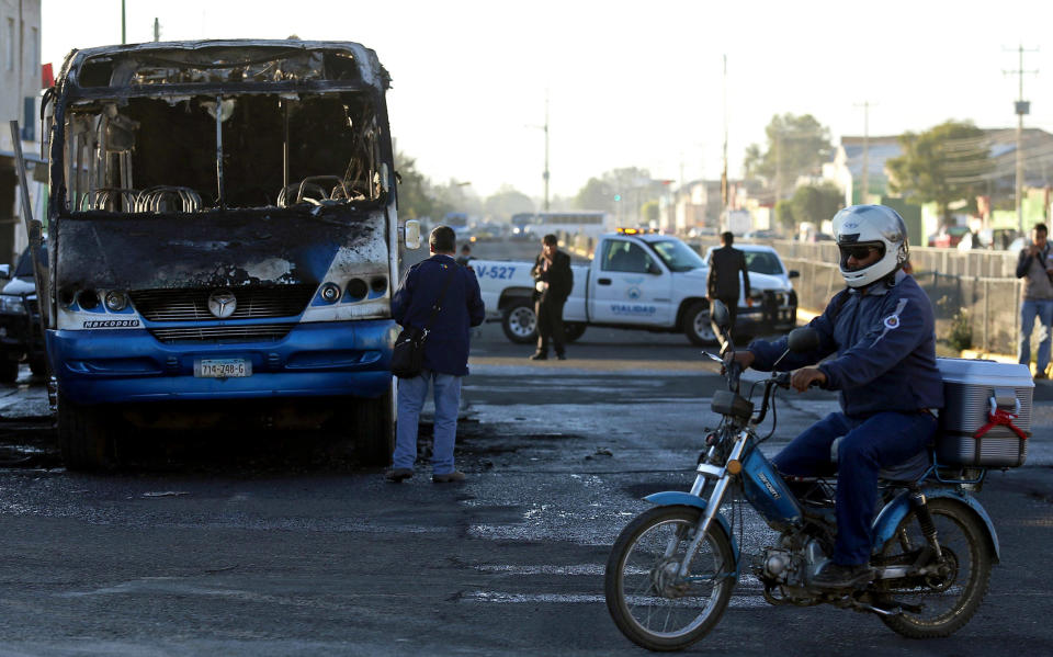 A motorcyclist drives by a burned bus in the town of Zapopan, Mexico, Thursday, Jan. 30, 2014. The bus was torched by unidentified attackers during a raid by officials who detained the son of an alleged leader of a drug cartel. A federal official who was not authorized to be quoted by name says the man detained is Ruben Oseguera. His father Nemesio Oseguera allegedly leads the Jalisco New Generation cartel. (AP Photo)