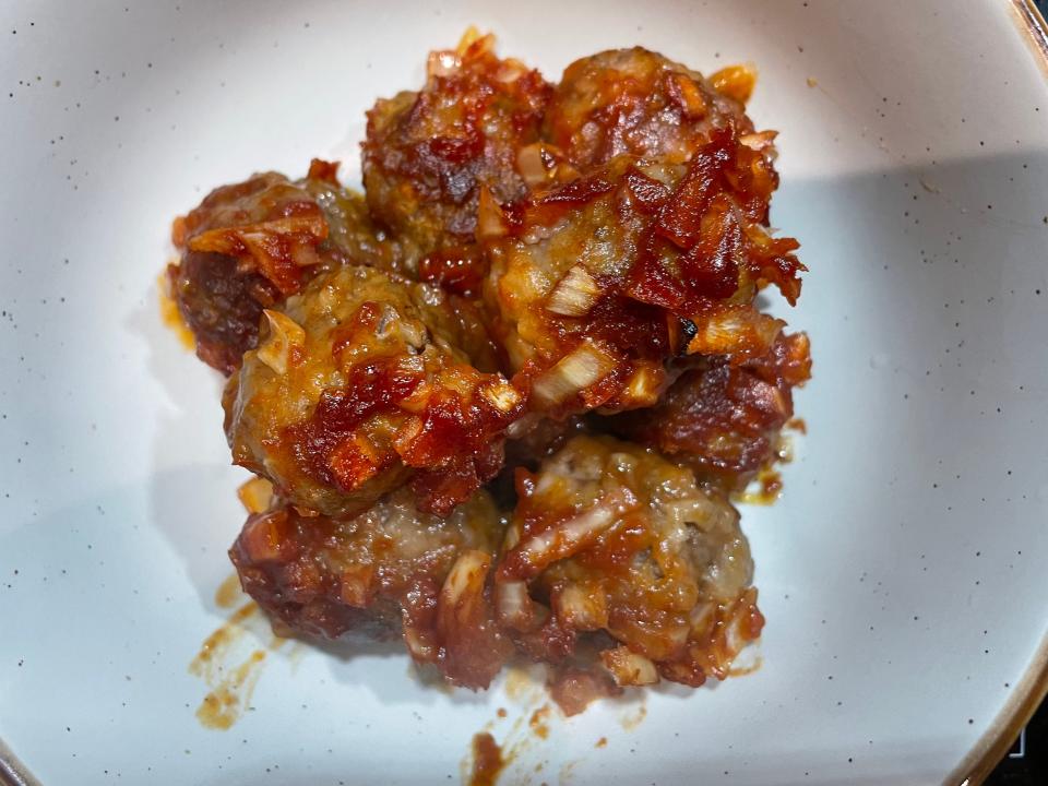 meatballs covered in an onion-tomato sauce in a ceramic bowl
