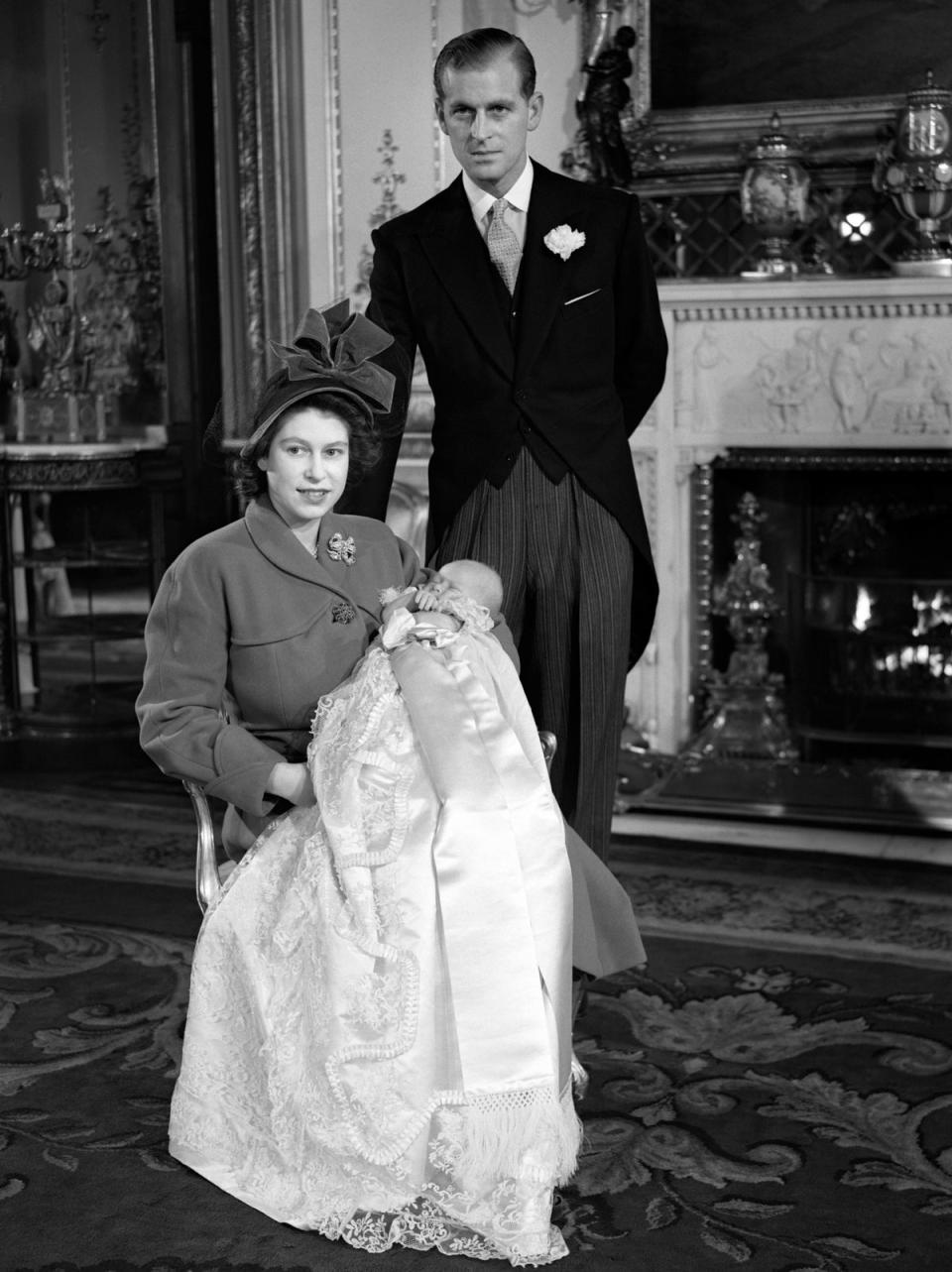 Princess Elizabeth holding Prince Charles in his Christening gown with her husband, the Duke of Edinburgh behind. (PA)