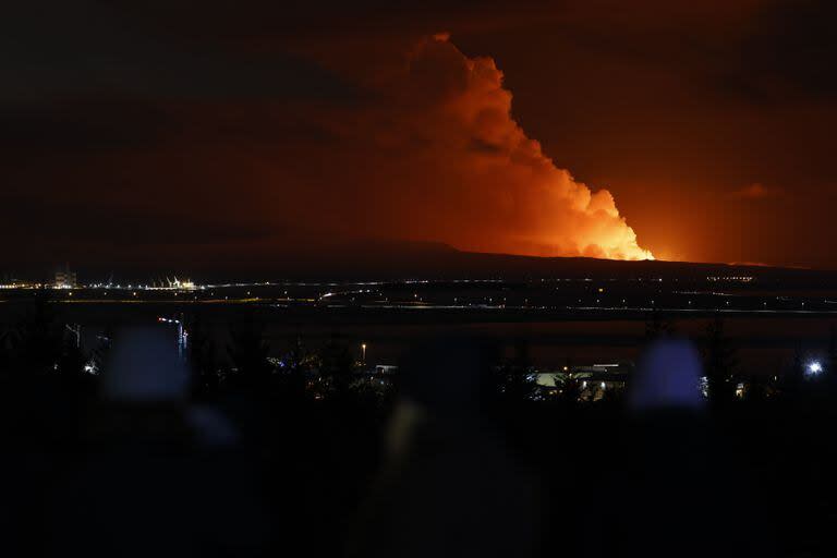 La gente observa cómo el cielo nocturno se ilumina debido a la erupción de un volcán en la península de Reykjanes, en el suroeste de Islandia, visto desde la ciudad capital de Reykjavik, el lunes 18 de diciembre de 2023.