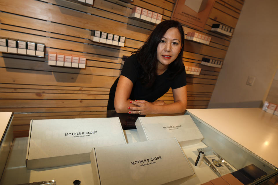 In this Friday, July 26, 2019 photo, Leslie Siu poses for a portrait next to her cannabis spray products geared toward women on display in Groundswell dispensary in east Denver. Pregnancy started out rough for her. Morning sickness and migraines had her reeling and barely able to function at a demanding New York marketing job, so like rising numbers of U.S. mothers-to-be, she turned to marijuana. “l was finally able to get out from under my work desk,” said Siu, who later started her own pot company and says her daughter, now 4, is thriving. (AP Photo/David Zalubowski)