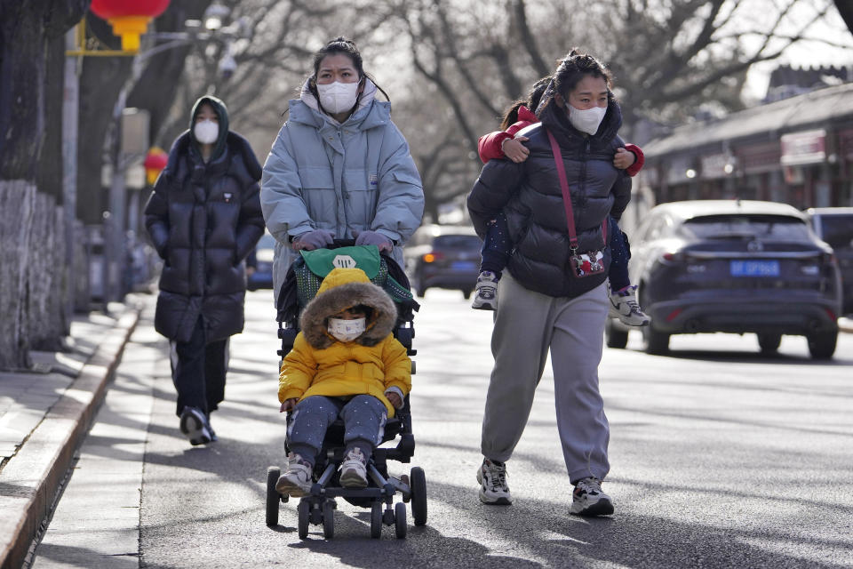 Women wearing face masks walk with their children on a street as they head to Forbidden City in Beijing, Tuesday, Jan. 17, 2023. China has announced its first population decline in decades as what has been the world's most populous nation ages and its birthrate plunges. (AP Photo/Andy Wong)