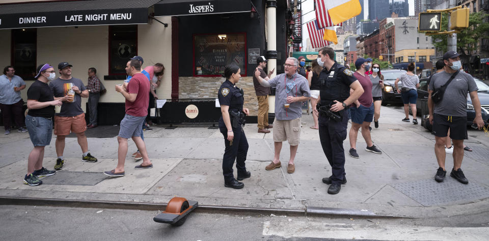 Police officers on patrol check on a small crowd outside a bar in the Hell's Kitchen neighborhood of New York, Friday, May 29, 2020, during the coronavirus pandemic. The street has been blocked off from traffic to allow residents to gather in open spaces with some social distancing. (AP Photo/Mark Lennihan)