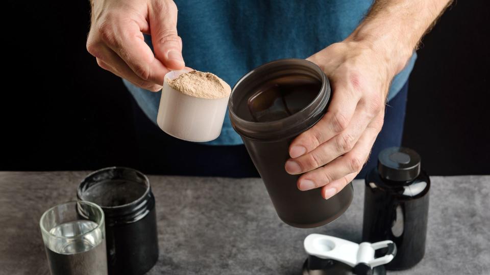 Man putting a scoop of protein powder into a protein shaker