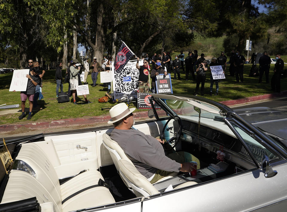 FILE - In this Feb. 27, 2021, file photo, a driver in his convertible cruises past a small group of anti-COVID-19 vaccine protesters demonstrating at Elysian Park, outside the Dodger Stadium vaccination mass center in Los Angeles. As the world struggles to break the grip of COVID-19, psychologists and misinformation experts are studying why the pandemic spawned so many conspiracy theories, which have led people to eschew masks, social distancing and vaccines. (AP Photo/Damian Dovarganes, File)