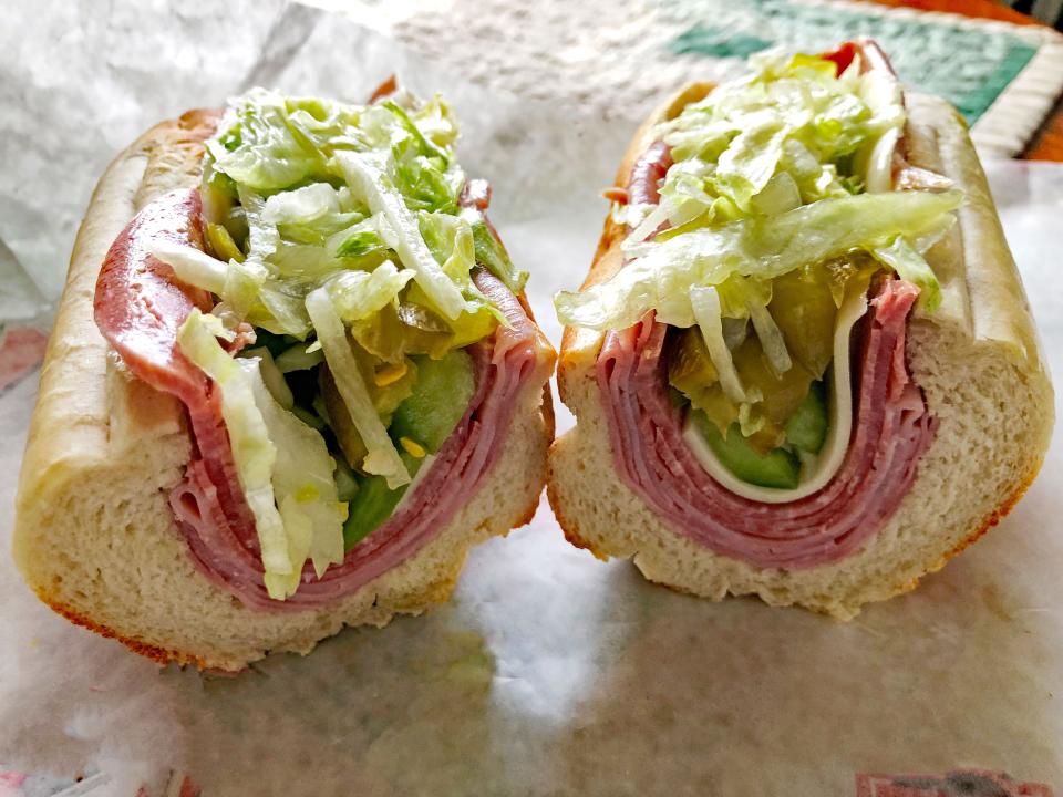 An Italian sub with ham, salami, cheese, lettuce, and pickles.