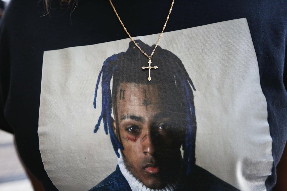 FILE- In this June 27, 2018, file photo a fan wears a cross around her neck dangling on a t-shirt in remembrance before she enters a memorial for the rapper, XXXTentacion in Sunrise, Fla. A Florida jury has convicted three men of murder in the 2018 killing of star rapper XXXTentacion, who was shot during a robbery that netted $50,000. The jury deliberated a little more than seven days before finding 28-year-old Michael Boatwright, 26-year-old Dedrick Williams and 24-year-old Trayvon Newsome guilty on Monday, March 20, 2023 of first-degree murder and armed robbery. (AP Photo/Brynn Anderson, File)