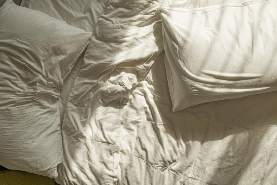 Crumpled white bed linens and pillows on an unmade bed. No people are present in the image