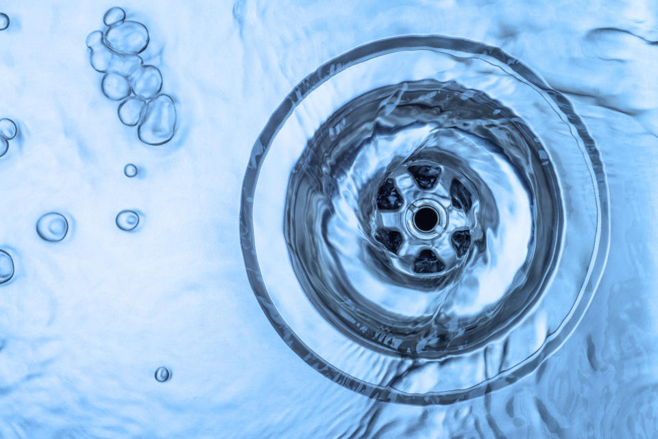 Water swirling down a drain with bubbles on the side