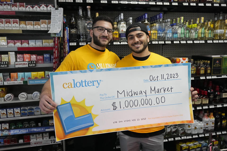 Jonathan Khalil, left, and Chris Khalil, sons of the store co-owners, hold up a ceremonial check presented to them by lottery officials at the Midway Market & Liquor store, Thursday, Oct. 12, 2023, in Frazier Park, Calif., where a $1.765 billion winning Powerball ticket was sold. (AP Photo/Marcio Jose Sanchez)