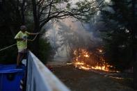 A man drops water to burning trees during a wildfire in Adames area, northern Athens, Greece, Tuesday, Aug. 3, 2021. Hundreds of residents living near a forest area north of Athens fled their homes Tuesday as a wildfire reached residential areas as Greece grappled with its worst heatwave in decades. (AP Photo/Michael Varaklas)