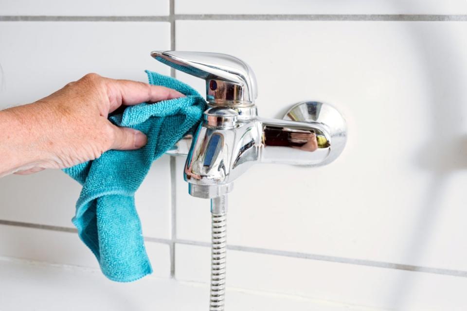 Person cleaning a bathtub faucet with a blue cloth.